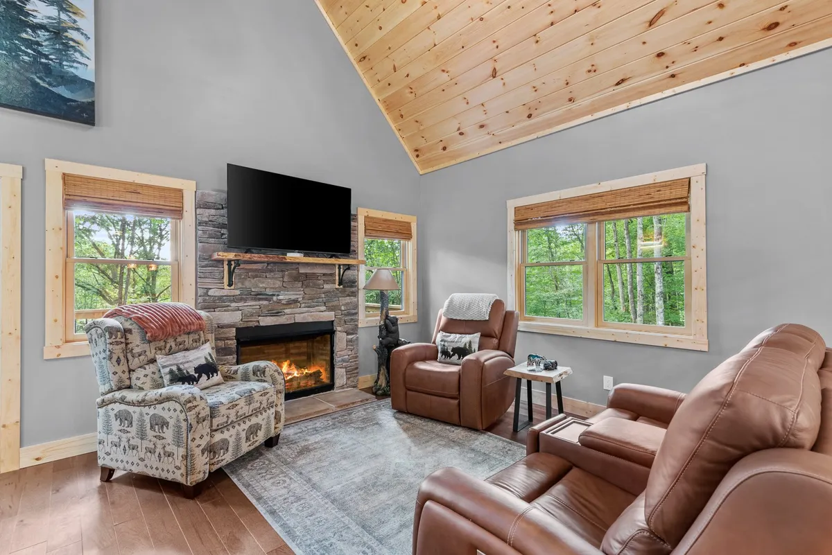 A cozy seating area is arranged around a gas log fireplace, with large windows framing views of the surrounding landscape. The space features warm wood finishes and plush sofas, offering an ideal spot for relaxing, watching TV, or enjoying game nights by the fire.