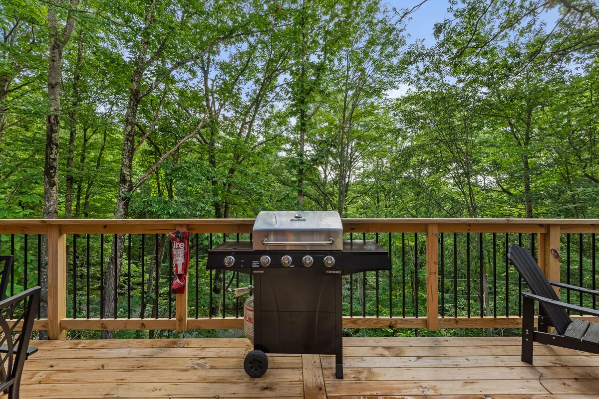 A wooden deck with a grill and outdoor dining area set amidst towering trees. The scene promises al fresco meals under open skies, surrounded by nature and the sounds of a distant creek or waterfall.
