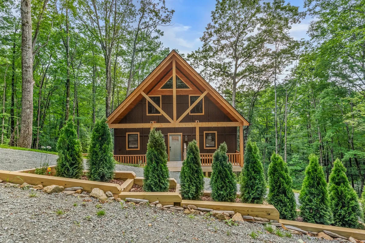 Showcasing the chalet-style cabin with an inviting front porch and a backdrop of evergreen trees, this image evokes the serenity of a mountain escape. The setting is ideal for family gatherings, nature walks, and quiet outdoor moments.