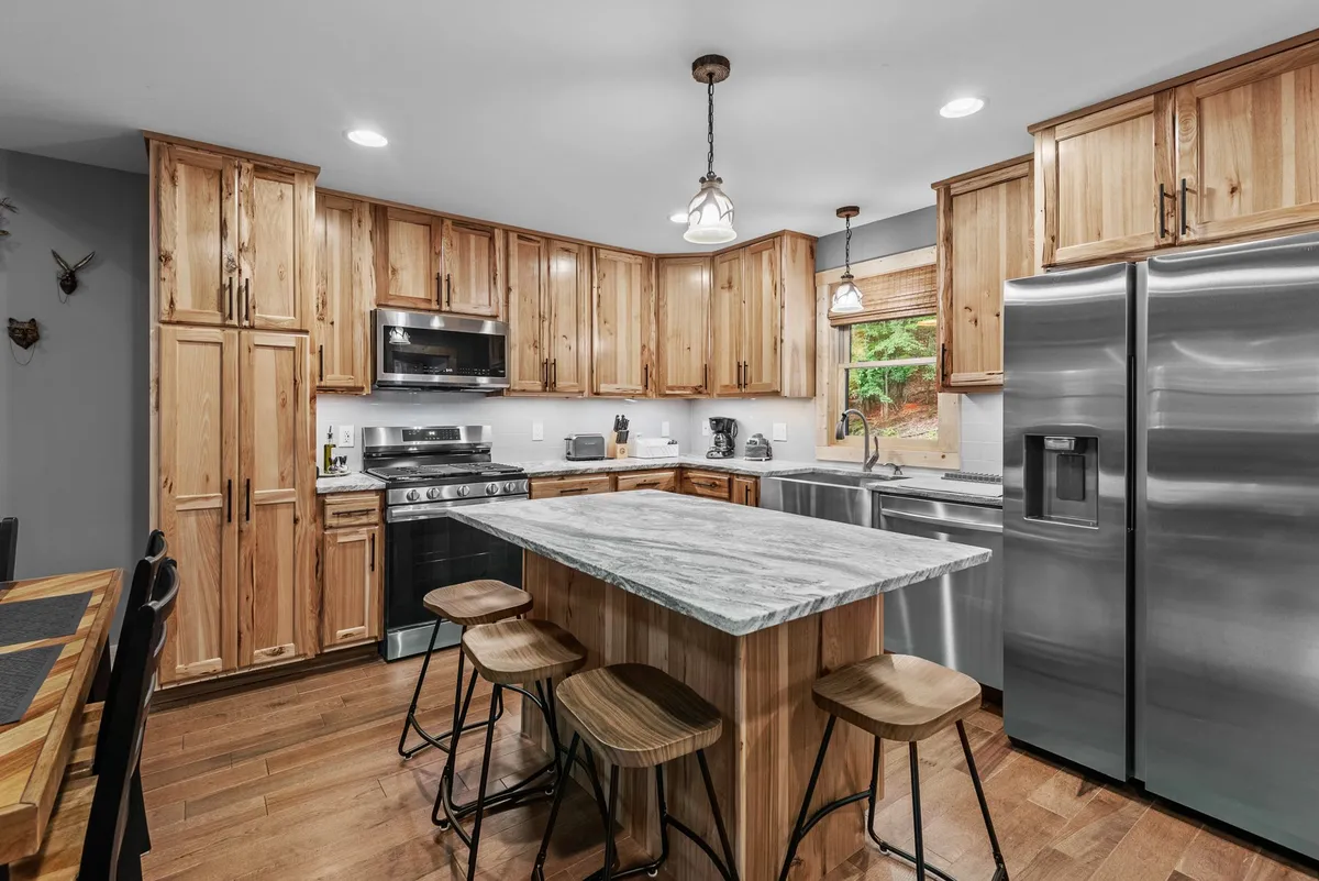A close-up angle of the kitchen area, featuring the island seating for three, stainless steel appliances, and custom wood cabinetry. The image emphasizes the culinary workspace and the inviting environment for meal prep and casual gatherings.