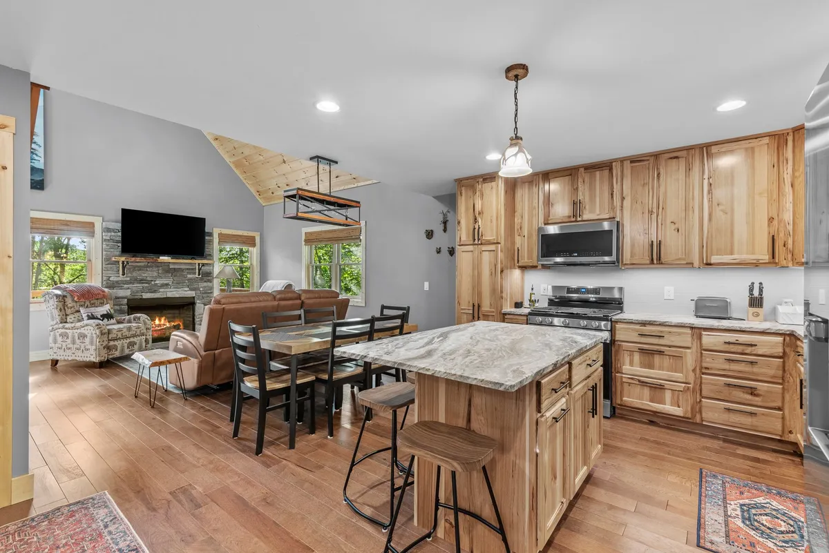 This image features an open-plan layout where the kitchen, dining area, and living space seamlessly flow together. The kitchen island, dining table, and a glimpse of the fireplace highlight communal spaces perfect for shared meals, game nights, and socializing.