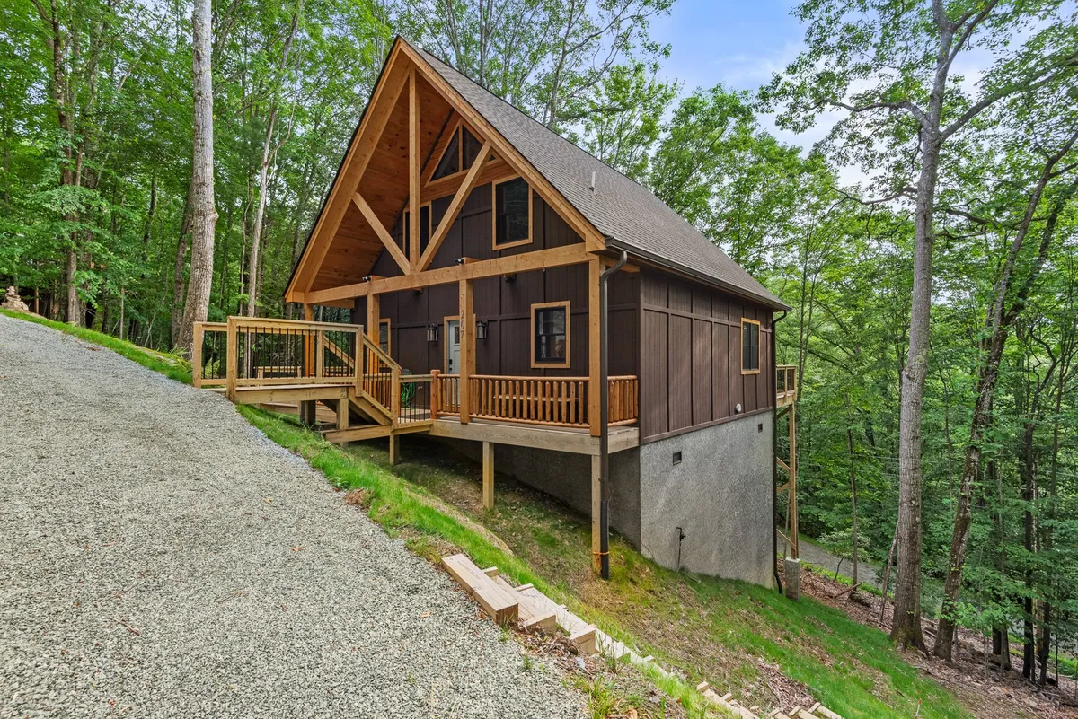 A striking A-frame cabin nestled among tall pines, featuring a spacious wooden deck surrounded by lush greenery. The inviting outdoor setting suggests seclusion and an ideal spot for couples to relax together, with the deck offering views of the forest and opportunities for wildlife sightings.