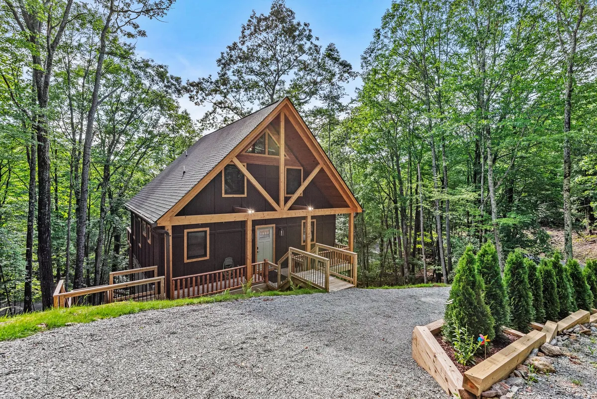 A wooden cabin sits amidst tall trees, with a landscaped path leading to the entrance. The porch area and natural surroundings invite guests to relax or set out on nearby nature walks.