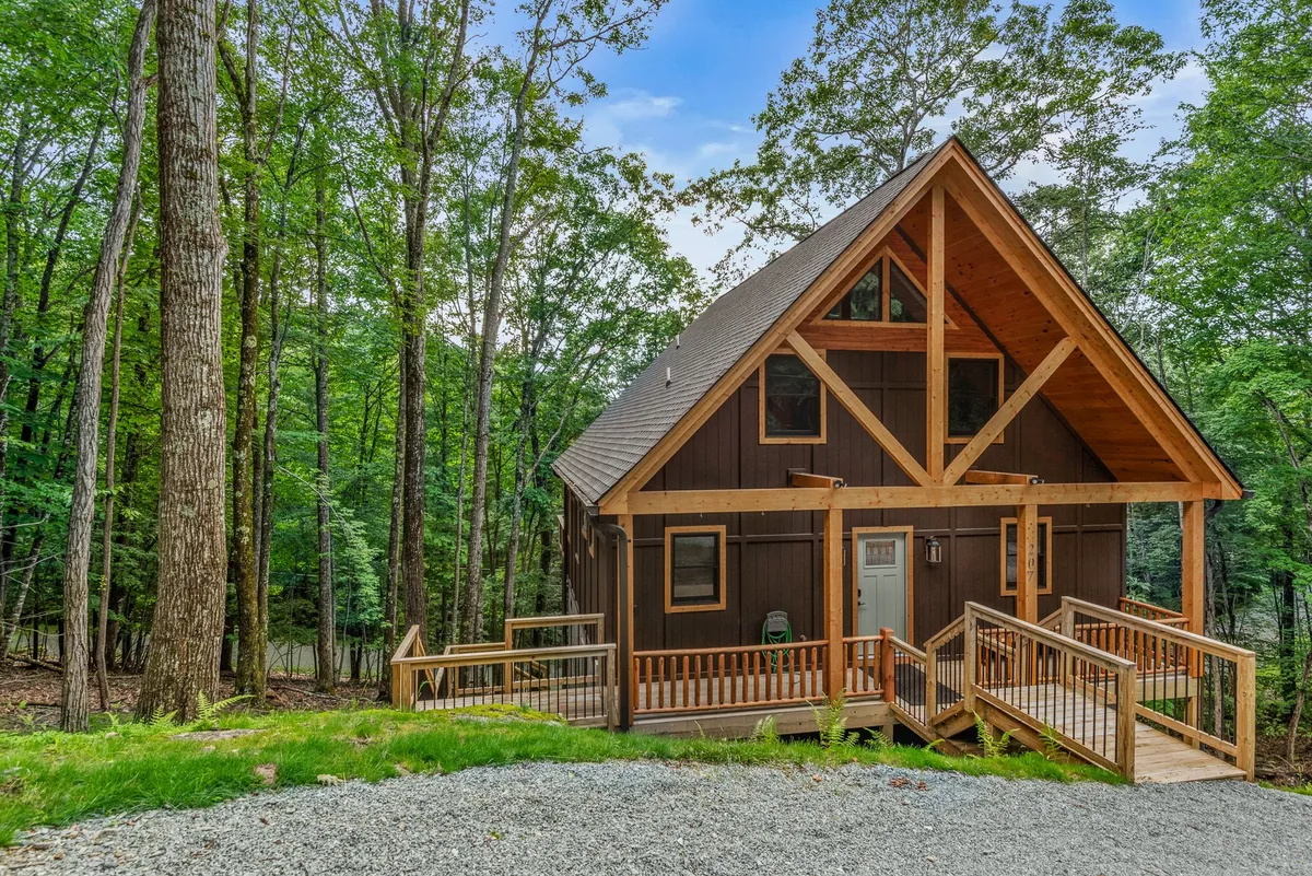 The image showcases a charming wooden cabin nestled among tall trees on picturesque Beech Mountain. The inviting deck, surrounded by lush greenery, offers a cozy space to unwind while taking in breathtaking sunset views or sipping coffee in the crisp mountain air.