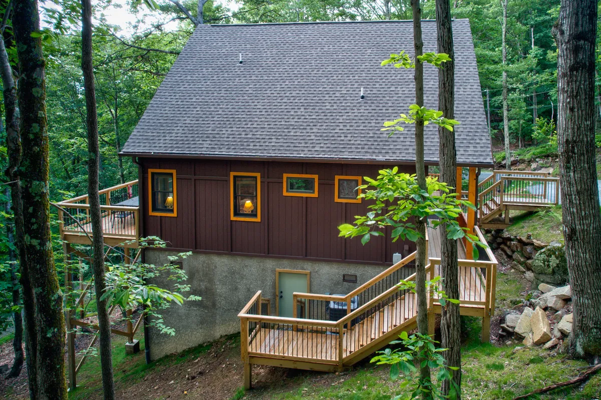 A peaceful wooden deck extends from the cabin, framed by large windows and set amidst natural greenery. The space offers a tranquil area for group gatherings and features enough room for evening chats or morning planning sessions, reinforcing the idea of connection to nature and group camaraderie.