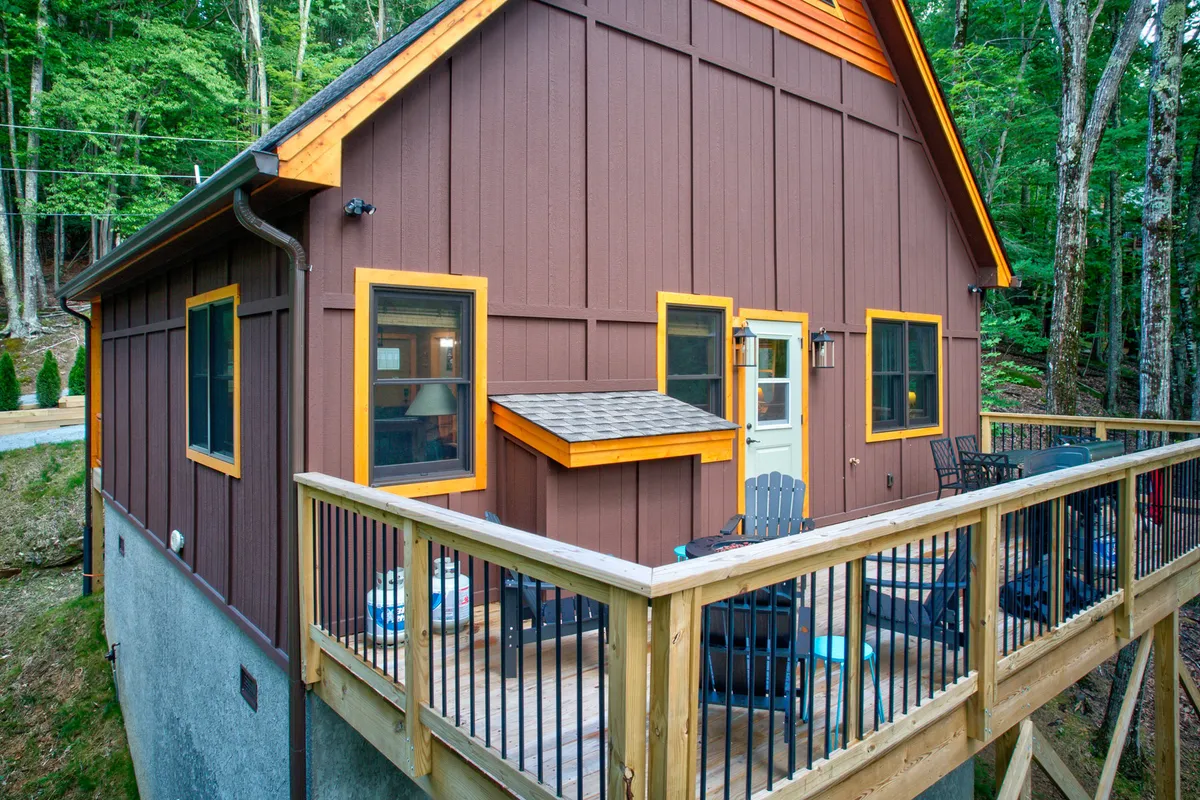 This image shows a cozy wooden deck with colorful window frames, surrounded by lush green trees. The outdoor seating area invites guests to relax and enjoy the natural mountain setting, suggesting the perfect spot for socializing, sharing drinks, or winding down after a day of adventure.