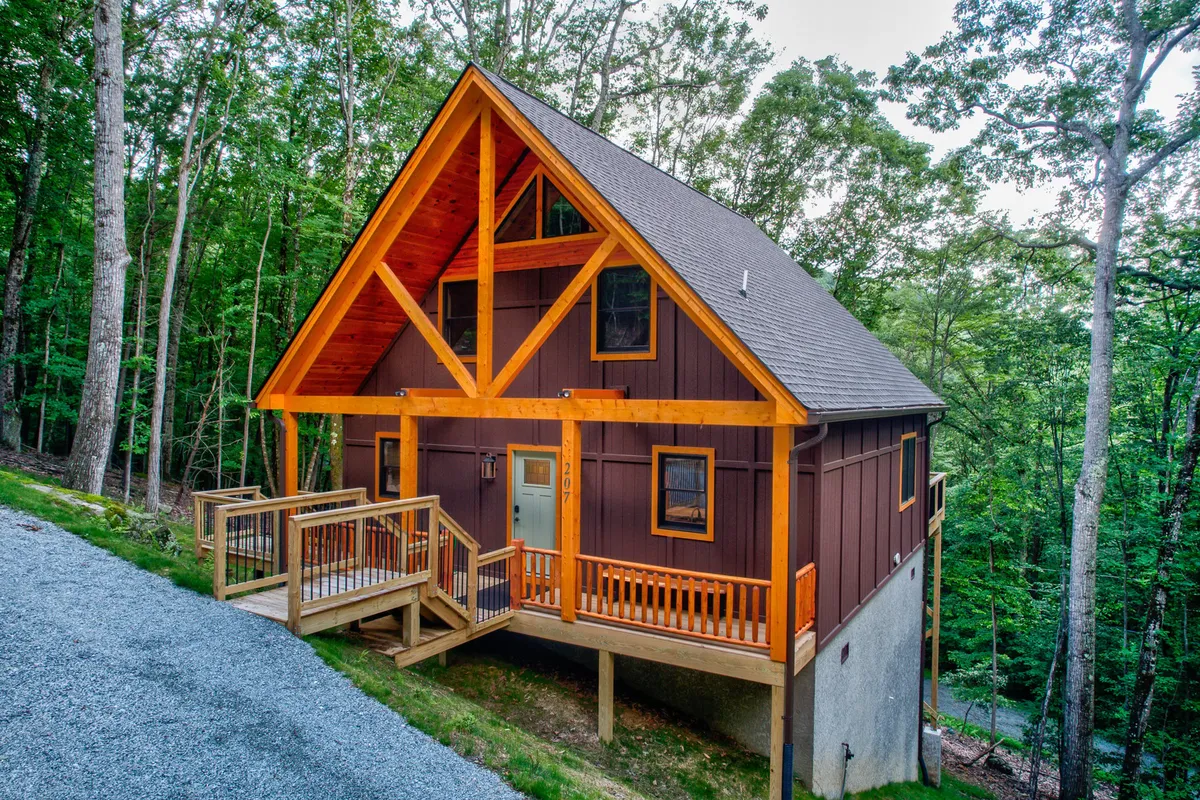 A cozy wooden deck with a striking triangular roof sits on a stone foundation, highlighted by large windows. The space is ideal for gatherings, relaxation, and taking in the scenery, especially at sunset.